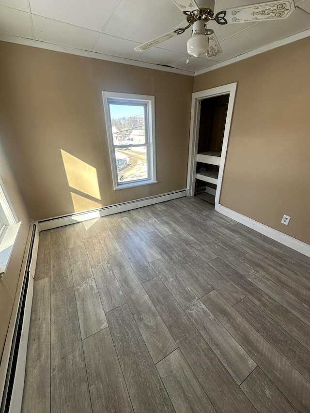 spare room featuring baseboards, a ceiling fan, ornamental molding, wood finished floors, and a baseboard heating unit