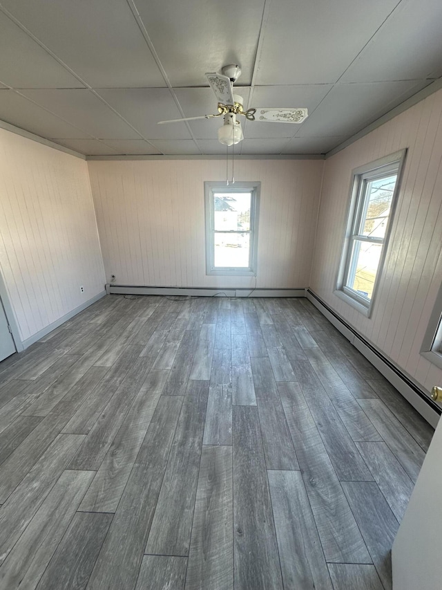 unfurnished room with a paneled ceiling, plenty of natural light, baseboard heating, and wood finished floors