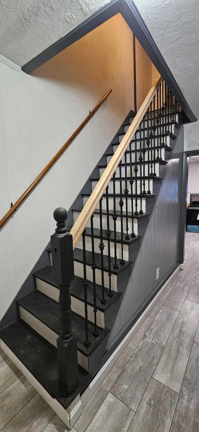 stairway with a textured ceiling, wood finished floors, and a decorative wall