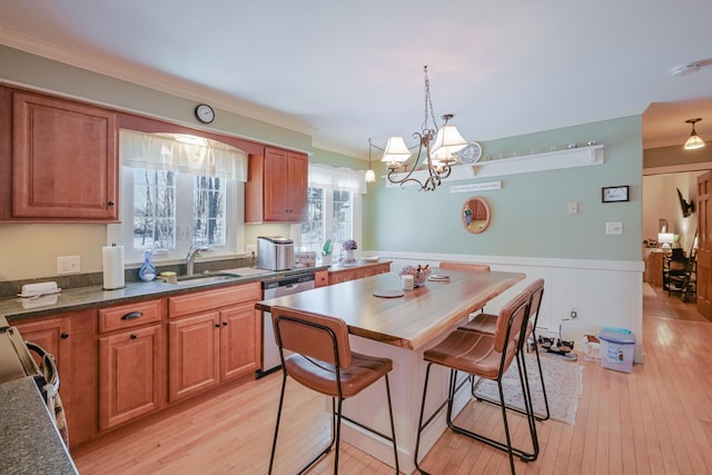 kitchen featuring dishwasher, sink, a breakfast bar area, hanging light fixtures, and light hardwood / wood-style floors