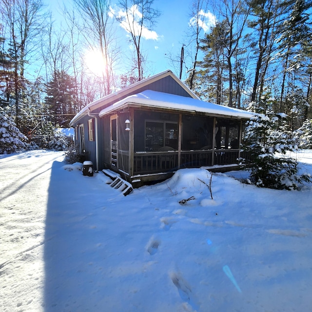 snow covered back of property featuring a sunroom