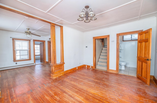 empty room with baseboard heating, wood-type flooring, and decorative columns