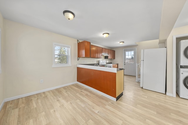 kitchen featuring stacked washing maching and dryer, light hardwood / wood-style floors, white appliances, and kitchen peninsula