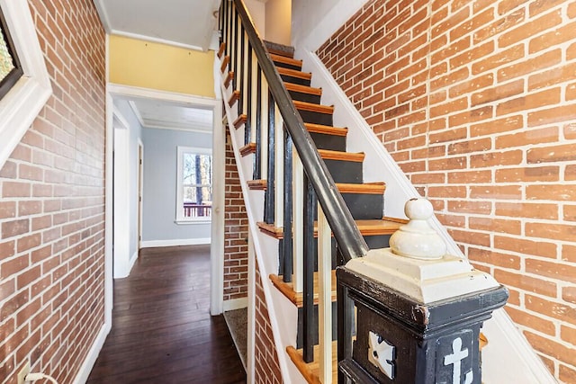 stairs featuring hardwood / wood-style flooring and brick wall