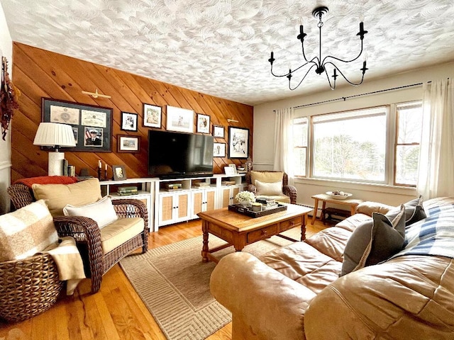 living room featuring wooden walls, a chandelier, light hardwood / wood-style floors, and a textured ceiling