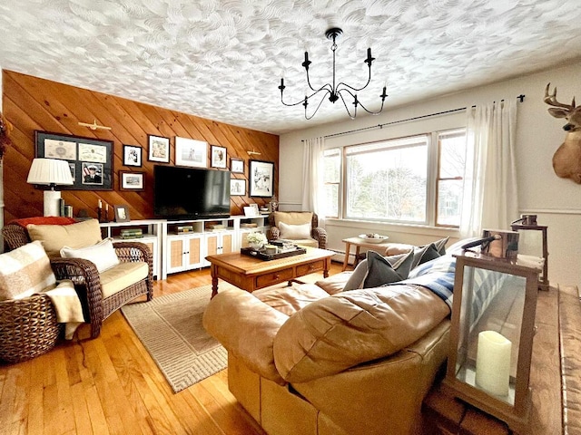 living room with an inviting chandelier, hardwood / wood-style floors, a textured ceiling, and wood walls