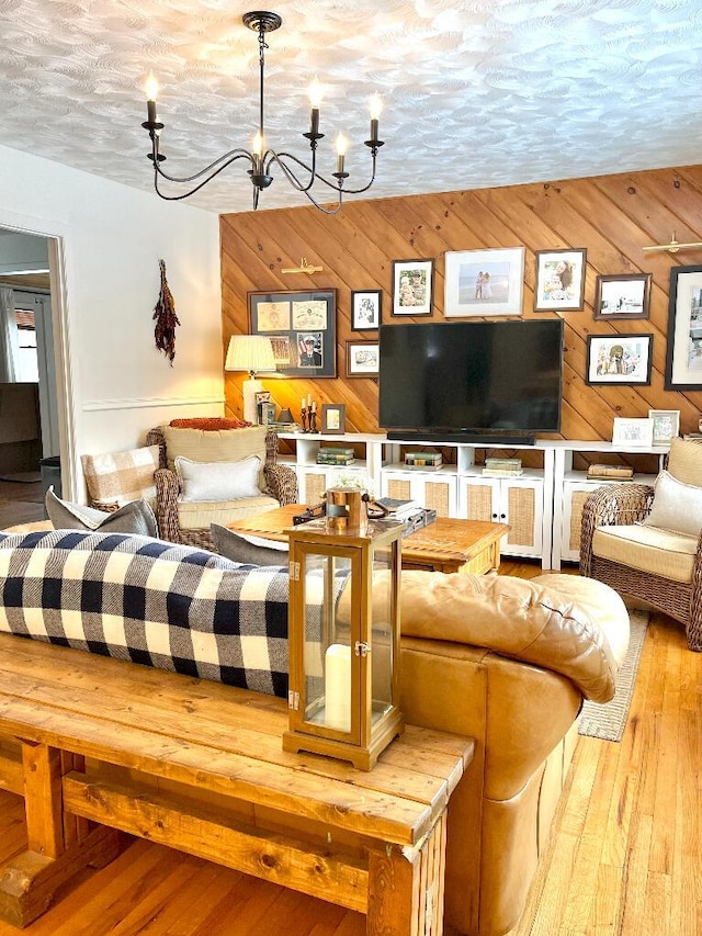 living room with an inviting chandelier, wood-type flooring, a textured ceiling, and wood walls