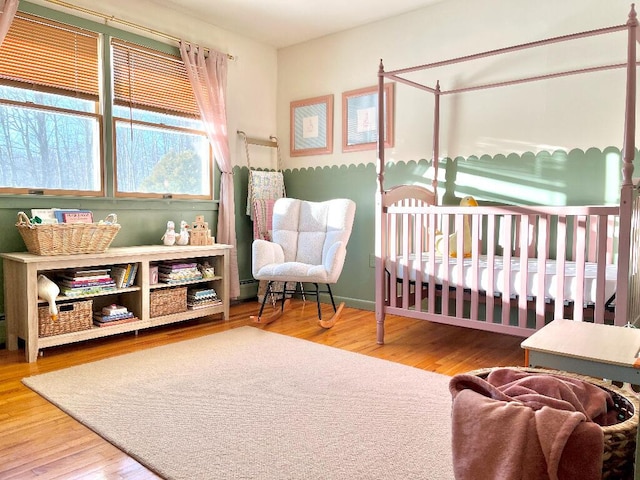 bedroom featuring hardwood / wood-style flooring, a baseboard radiator, and a nursery area