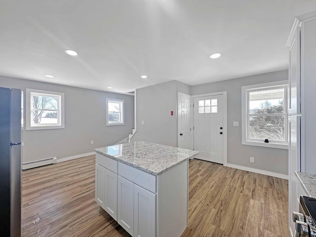 kitchen with stainless steel refrigerator, white cabinets, a baseboard heating unit, light stone countertops, and light wood-type flooring