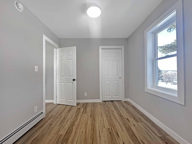 unfurnished bedroom featuring a closet, light hardwood / wood-style flooring, and a baseboard heating unit