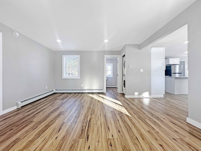 unfurnished living room with a baseboard radiator, stacked washer / dryer, and light hardwood / wood-style floors