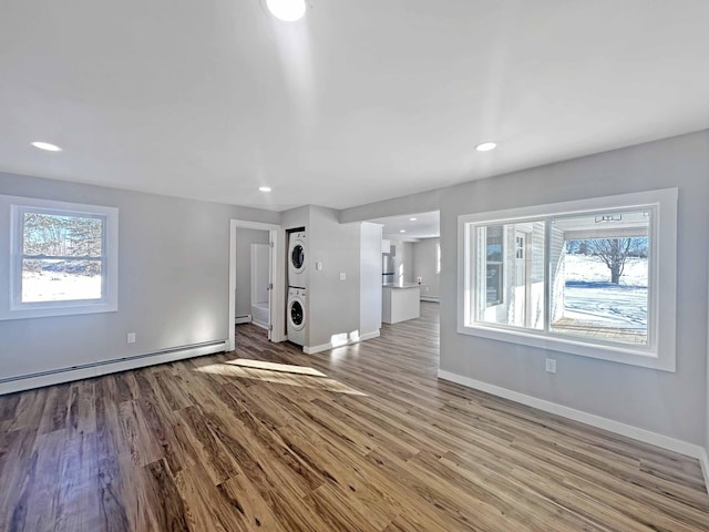 unfurnished living room with light hardwood / wood-style floors, baseboard heating, and stacked washing maching and dryer