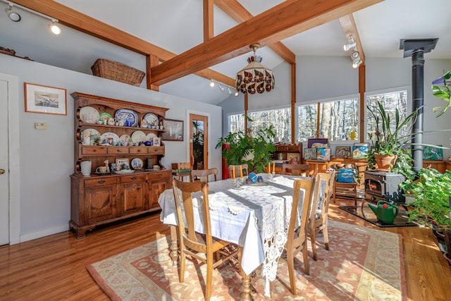 dining area featuring a wood stove, vaulted ceiling with beams, track lighting, and light hardwood / wood-style flooring