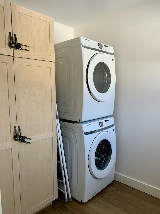 washroom with dark hardwood / wood-style flooring, stacked washer and dryer, and cabinets