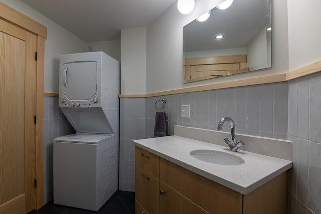 bathroom featuring tile patterned floors, vanity, stacked washing maching and dryer, and tile walls