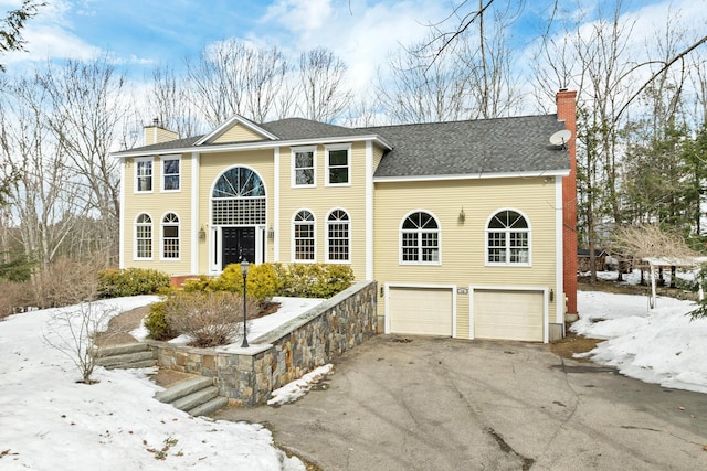 view of front of house with aphalt driveway, an attached garage, roof with shingles, and a chimney