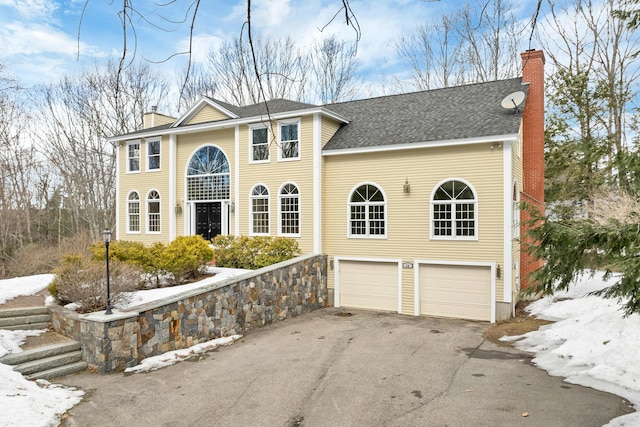 view of front of property featuring aphalt driveway, an attached garage, a chimney, and a shingled roof