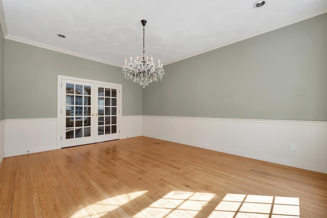 spare room with a wainscoted wall, light wood-style floors, french doors, crown molding, and a notable chandelier