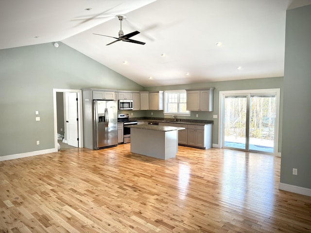 kitchen with dark countertops, a kitchen island, stainless steel appliances, light wood-type flooring, and high vaulted ceiling