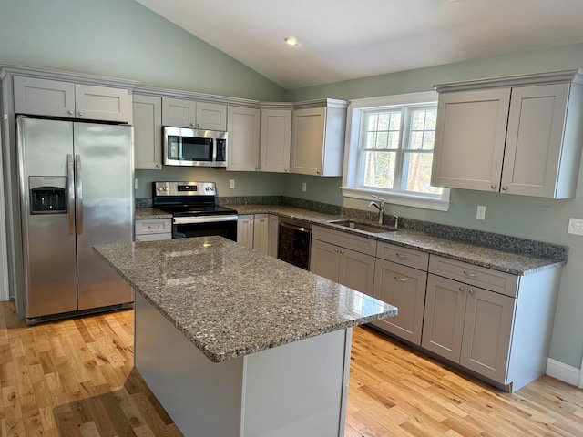 kitchen with gray cabinetry, stainless steel appliances, a sink, vaulted ceiling, and light wood-type flooring