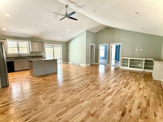 unfurnished living room featuring light wood finished floors, baseboards, a baseboard heating unit, and a sink