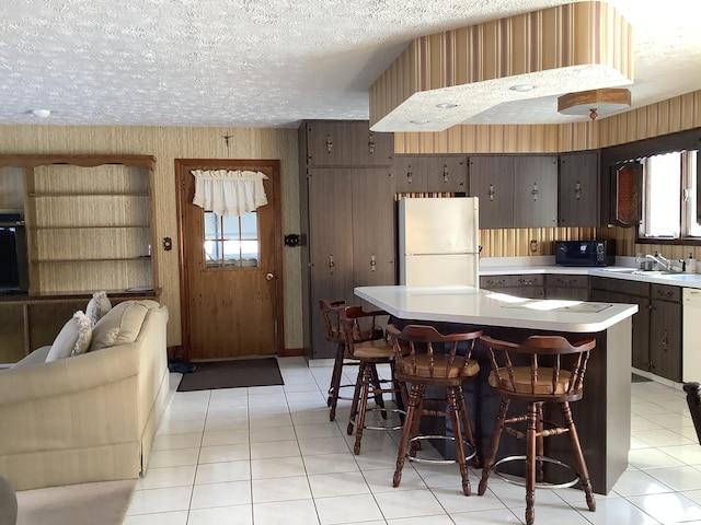 kitchen featuring sink, a breakfast bar area, white refrigerator, dark brown cabinetry, and a textured ceiling