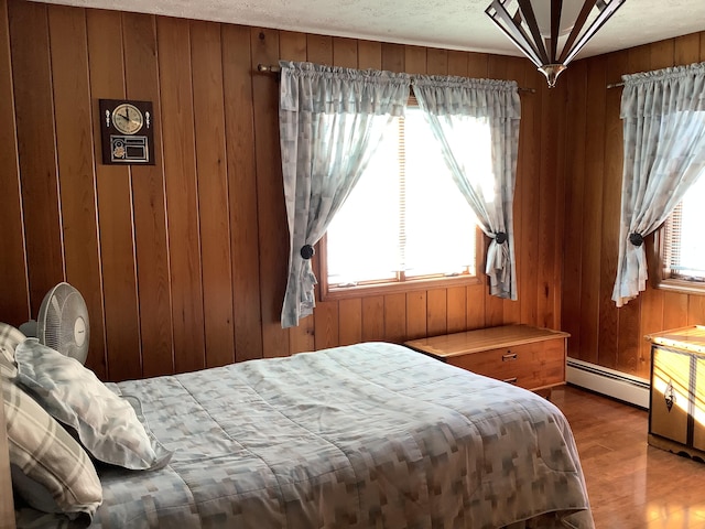 bedroom featuring multiple windows, wood-type flooring, a baseboard heating unit, and wood walls