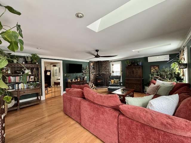 living room with a skylight, a wood stove, a wall mounted AC, ornamental molding, and light hardwood / wood-style flooring