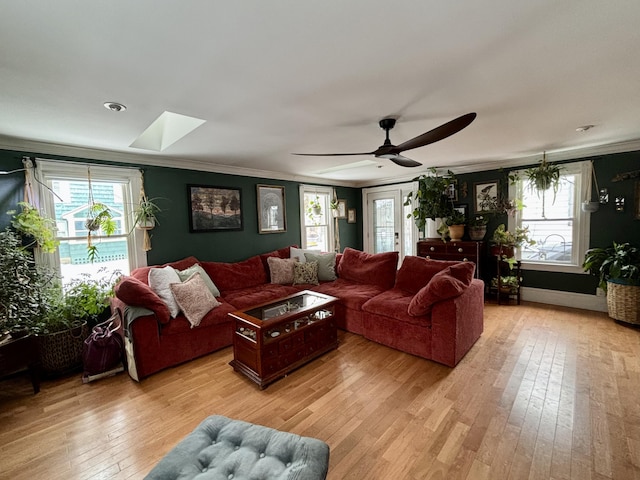 living room with crown molding, a skylight, ceiling fan, and light wood-type flooring