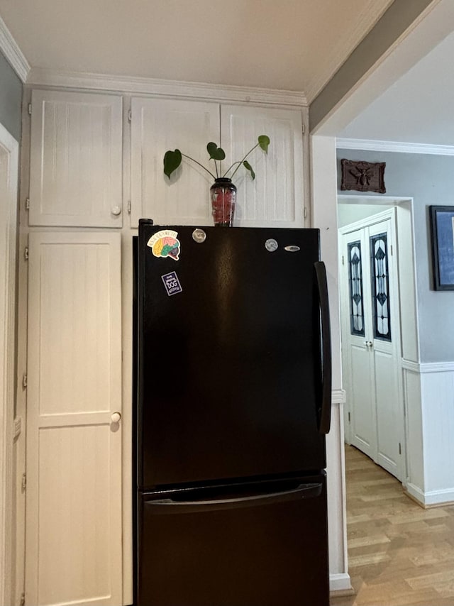 details with black refrigerator, crown molding, light hardwood / wood-style floors, and white cabinets