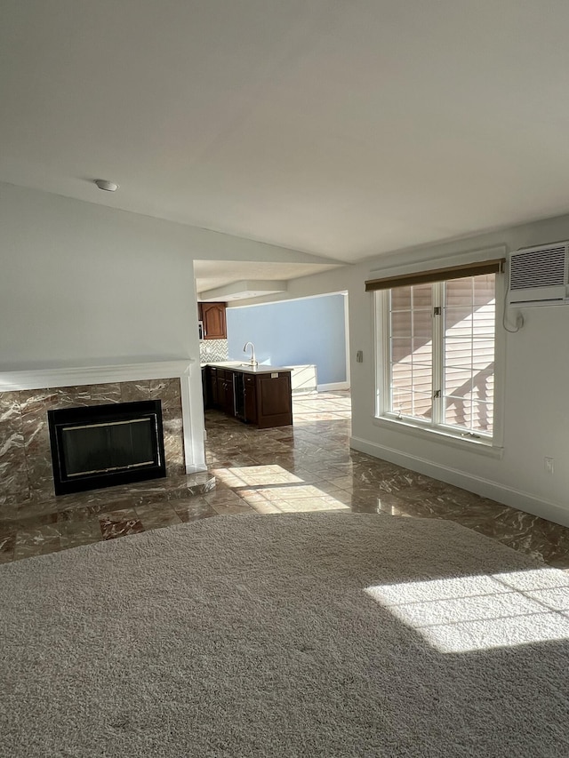 unfurnished living room featuring sink, a wall unit AC, carpet, a fireplace, and vaulted ceiling