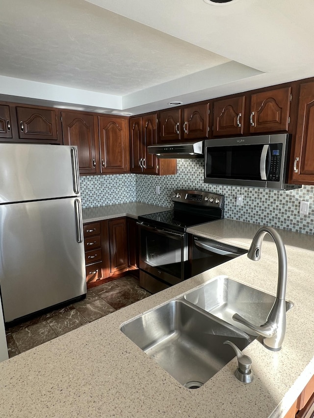 kitchen with sink, backsplash, range hood, stainless steel appliances, and a tray ceiling