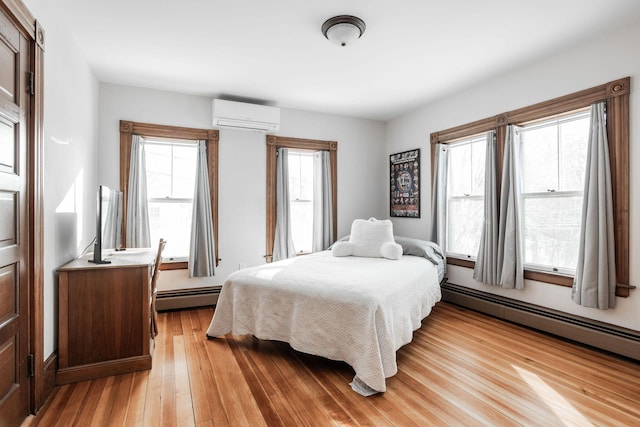 bedroom with a baseboard heating unit, light hardwood / wood-style flooring, and an AC wall unit