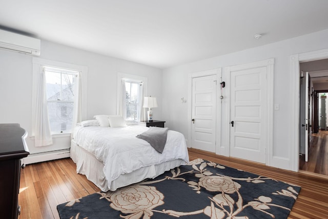 bedroom featuring an AC wall unit, light hardwood / wood-style floors, and a baseboard heating unit