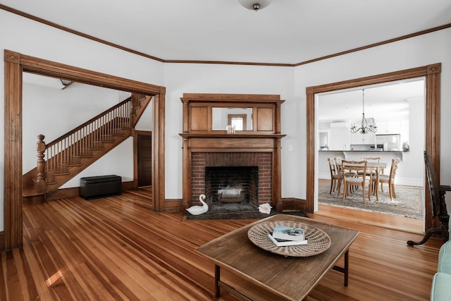 living room with crown molding, a brick fireplace, hardwood / wood-style flooring, and a chandelier