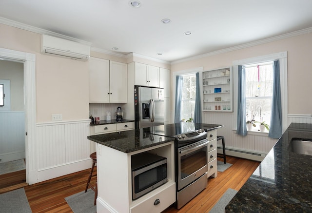 kitchen featuring appliances with stainless steel finishes, white cabinetry, a baseboard radiator, an AC wall unit, and light wood-type flooring