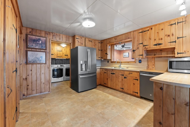 kitchen featuring sink, wooden walls, stainless steel appliances, tasteful backsplash, and washing machine and clothes dryer