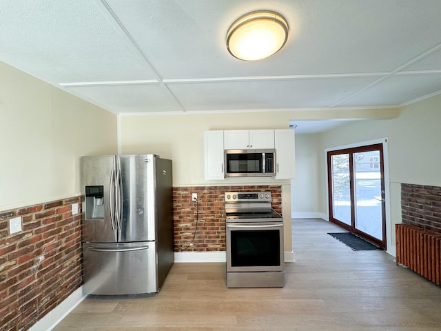 kitchen featuring white cabinetry, brick wall, stainless steel appliances, and light wood-type flooring