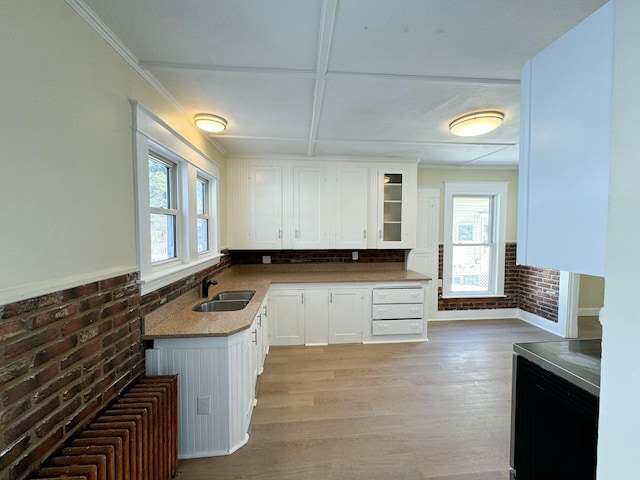 kitchen featuring sink, light hardwood / wood-style flooring, white cabinets, and brick wall