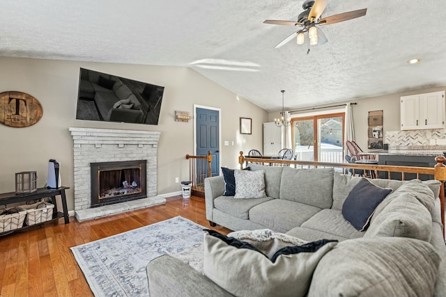 living room featuring lofted ceiling, a fireplace, a textured ceiling, ceiling fan with notable chandelier, and light wood-type flooring