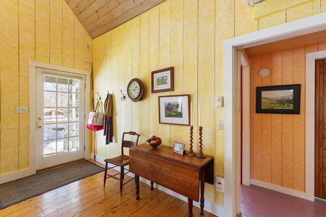 entryway with vaulted ceiling, hardwood / wood-style floors, and wood walls