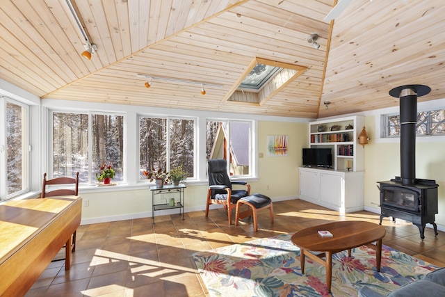 interior space featuring wooden ceiling, rail lighting, vaulted ceiling with skylight, and a wood stove