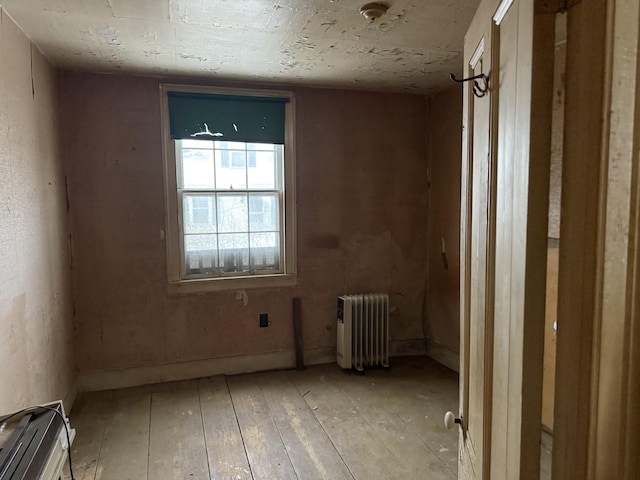 spare room with radiator heating unit, light wood-type flooring, and baseboards