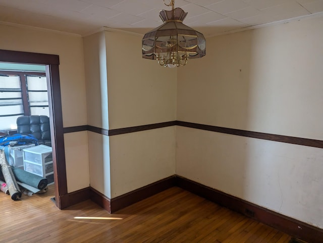 empty room featuring baseboards, hardwood / wood-style floors, a chandelier, and crown molding