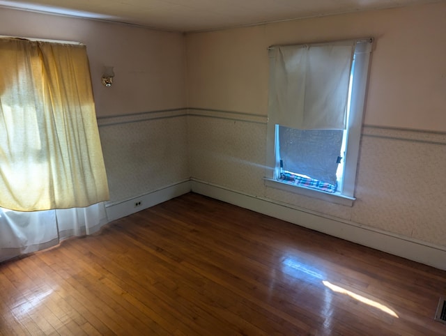 empty room featuring hardwood / wood-style floors, wainscoting, and visible vents