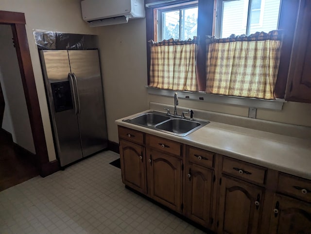 kitchen with stainless steel refrigerator with ice dispenser, light floors, light countertops, a wall mounted AC, and a sink