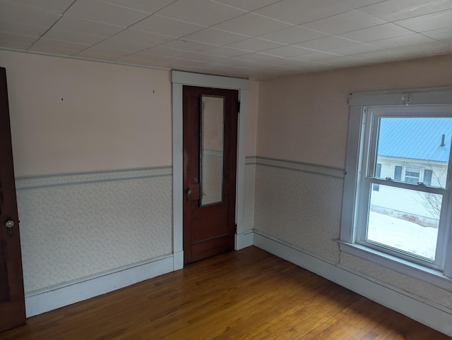 unfurnished room with a paneled ceiling, a wainscoted wall, wood finished floors, baseboards, and wallpapered walls