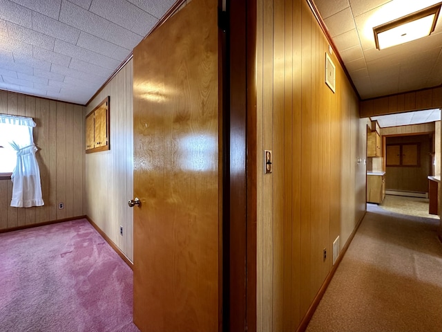 hallway featuring baseboard heating, light colored carpet, and wood walls