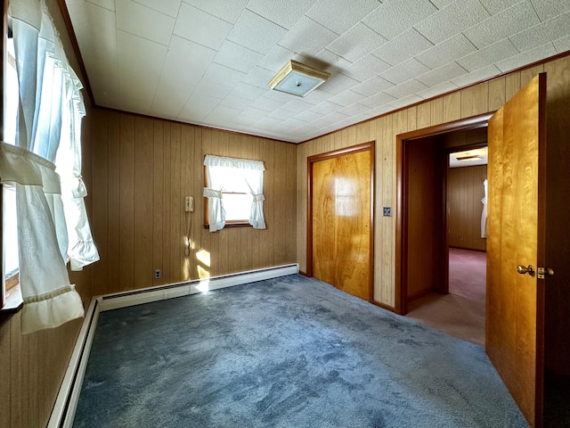 carpeted empty room featuring a baseboard heating unit and wood walls