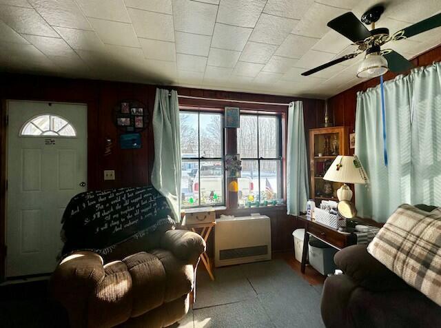 living area featuring ceiling fan and wood walls